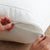 Close-up of hands unzipping the PureCare StainGuard® Cotton Terry Pillow Protector by PureCare, showing the inner pillow against a beige quilted background. The person has short nails with light pink polish.
