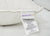 The Down Etc. 25% White Goose Down / 75% White Goose Feather Pillow has a white cotton cover with several seam tags, including a top "Down Etc." tag in purple and gold, and others showing materials, care info, and a barcode.