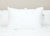 A large, fluffy Sysco Guest Supply Dream Escape Down Alternative Pillow (formerly Dream Essence) is centered on a white quilted bedspread, with clean linens and a hypoallergenic design that creates a fresh, inviting look against the light beige wall.