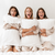 Three women in white robes sitting on a bed with Hollander Holiday Inn<sup>®</sup> Soft Support Pillow Combo Pack | Polyester and Down & Feather (Includes 2 Pillows), providing each other support.